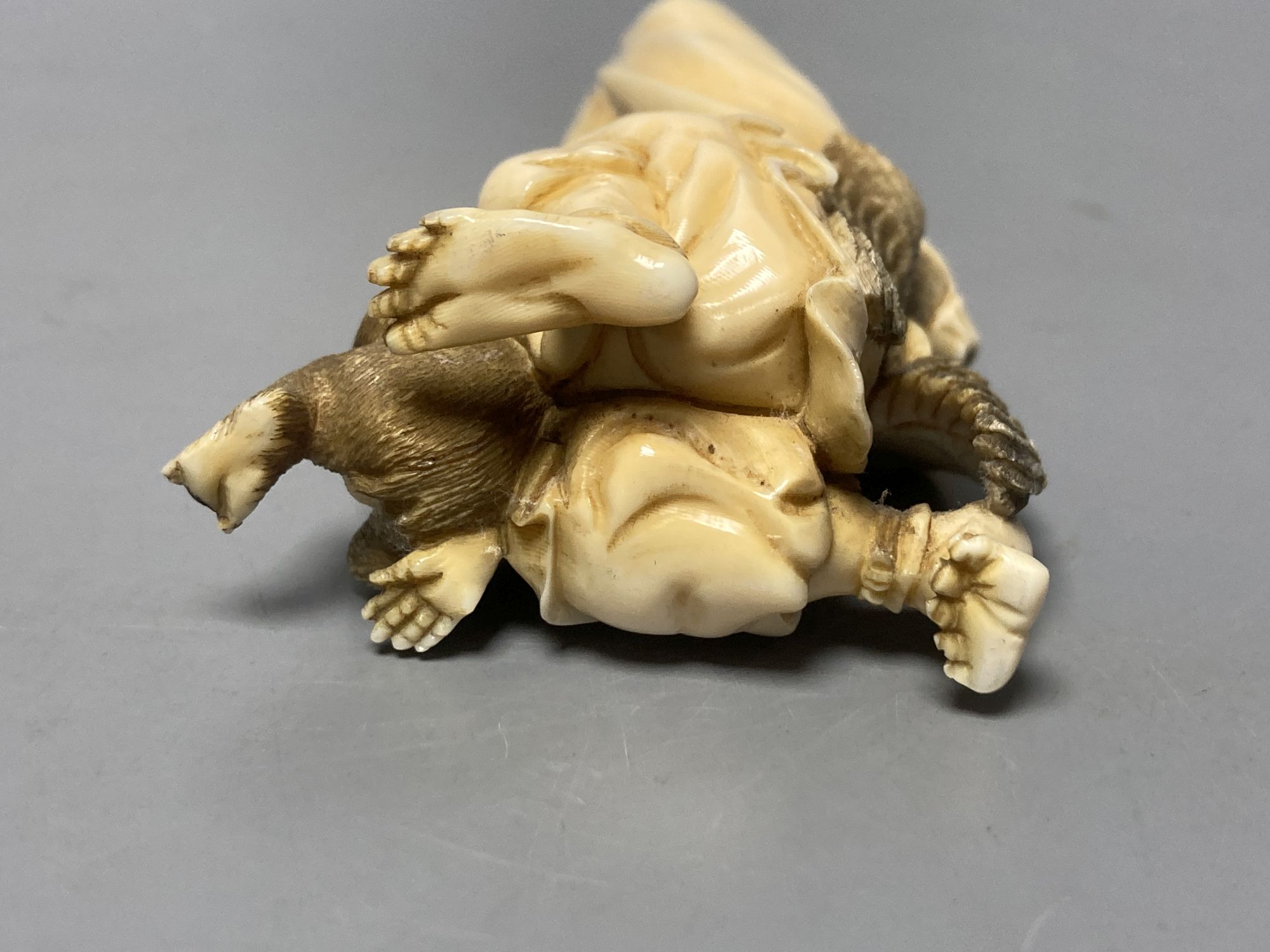 A Japanese ivory okimono of a winged man blowing a conch, monkey below, Meiji, 89 grams